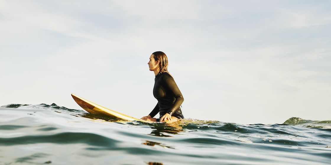 wide shot of female surfer sitting on surfboard in ocean while waiting for wave during sunrise surf session
