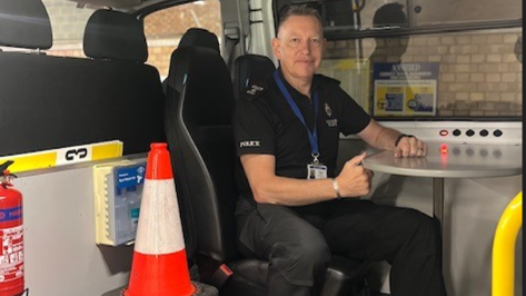 Sgt Hatch sitting inside a police van with a road traffic cone beside him