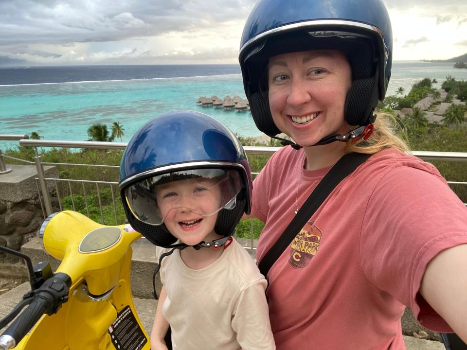 Mother and son wearing helmets on motorbike with ocean in the background.