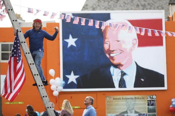 A man puts a U.S. flag up in the town of Ballina, the ancestral home of President elect Joe Biden, in North West of Ireland, Saturday, Nov. 7, 2020, after Biden was elected president.