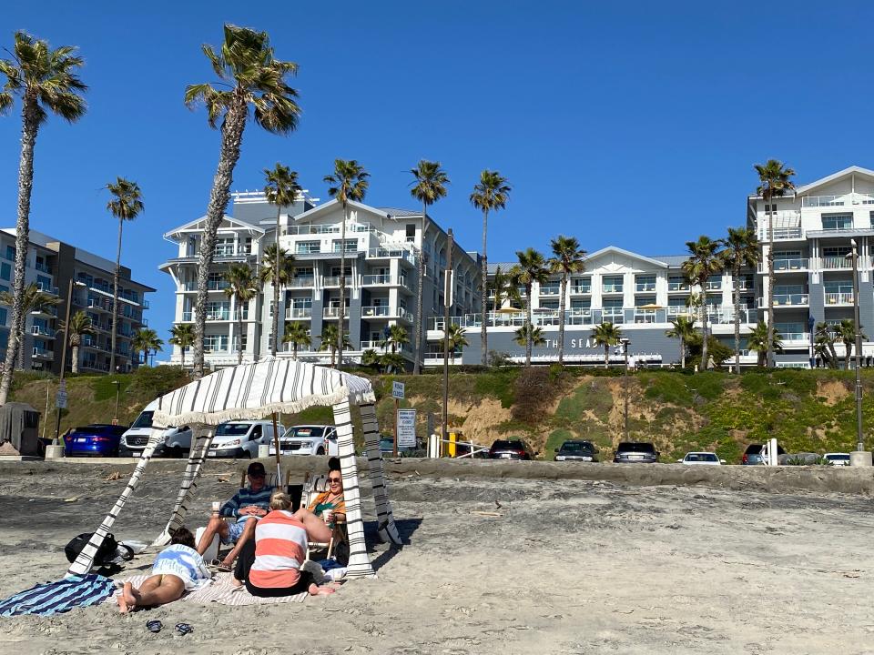 Vacationers set up a cabana and relax on Oceanside’s wide sandy beach. Fluttering palms frame The Seabird Ocean Resort, a luxury accommodation on Pacific Street across from the Strand. The California vacation destination has more than three miles of beach.