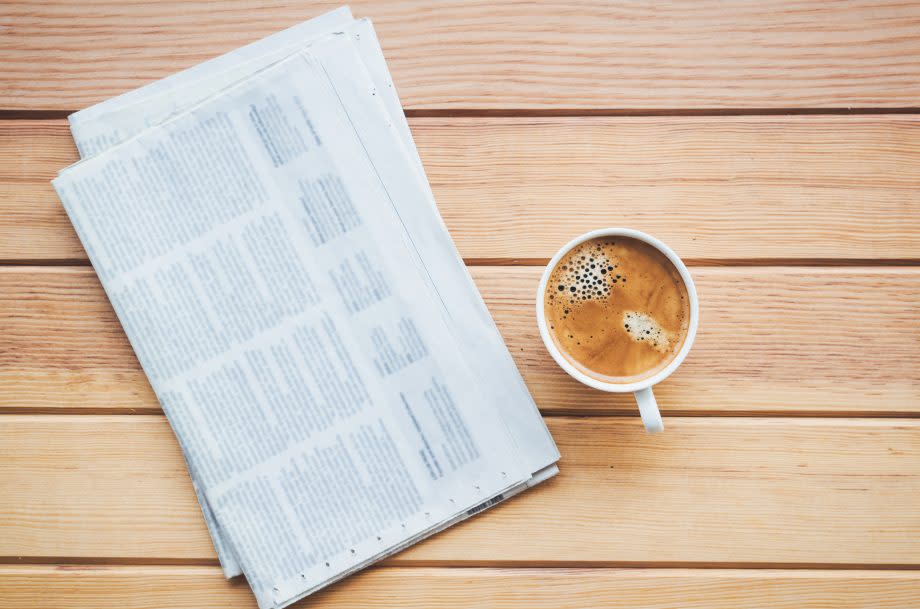 Eine Zeitung liegt zusammen mit einer Kaffeetasse auf einem Tisch.