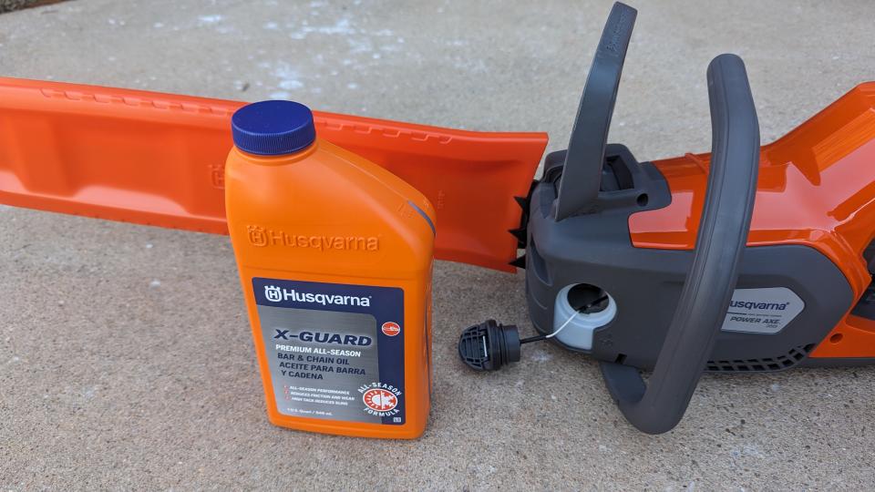 Image showing a bottle of chain oil, next to the chainsaw, where the oil cap is open ready for oil to be poured in