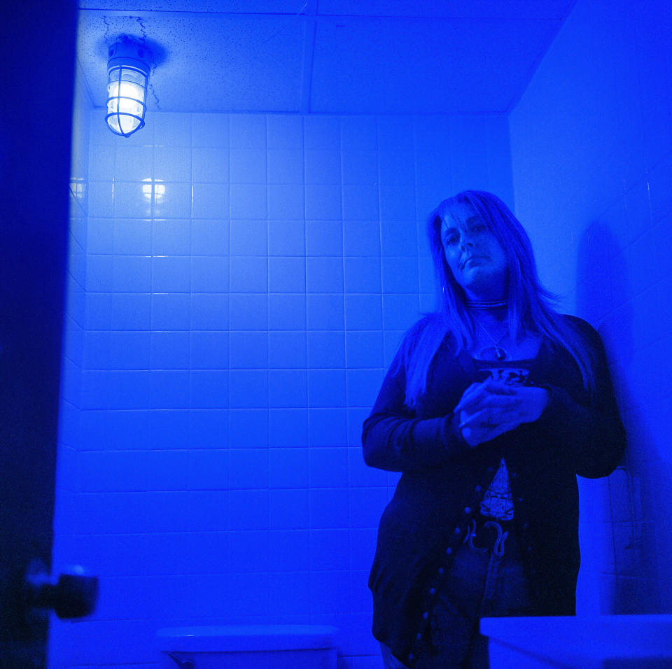 In this photo made with a medium format film camera, Misti Mann-France stands for a portrait in a bathroom at the laundromat she manages under a blue light installed to make it harder for drug users to find a vein, Thursday, March 18, 2021, in Huntington, W.Va. Hers was among several local businesses to install blue lights at the height of the city's opioid crisis, when they would often find syringes left behind by drug users. "It was the only thing we could think of to do to help," she said. "And it has helped tremendously." She said people have overdosed several times in the parking lot of their business, which includes the laundry and a video poker room. A local gas station chain and liquor store also switched to blue lights. "I wish there was a solution to the bigger problem," she said. "There are so many out there on drugs, and it's sad, it really is." (AP Photo/David Goldman)