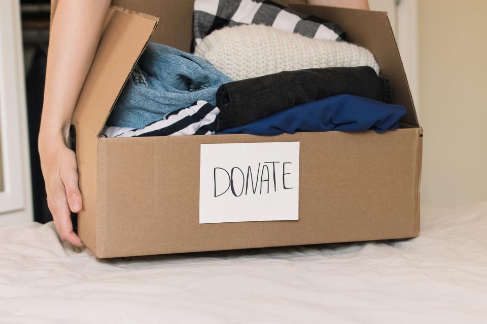 swedish death cleaning, woman's hands holding a box full of clothes to donate