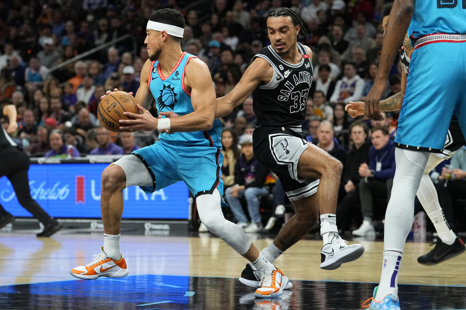 Phoenix Suns guard Devin Booker rebounds as San Antonio Spurs guard Tre Jones (33) defends during the first half of an NBA basketball game, Tuesday, April 4, 2023, in Phoenix. (AP Photo/Matt York)