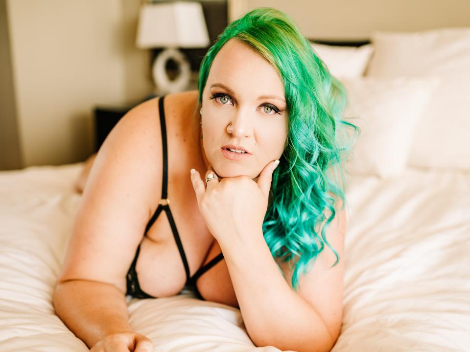 A plus-size woman in lingerie poses on a bed for a boudoir photography session.