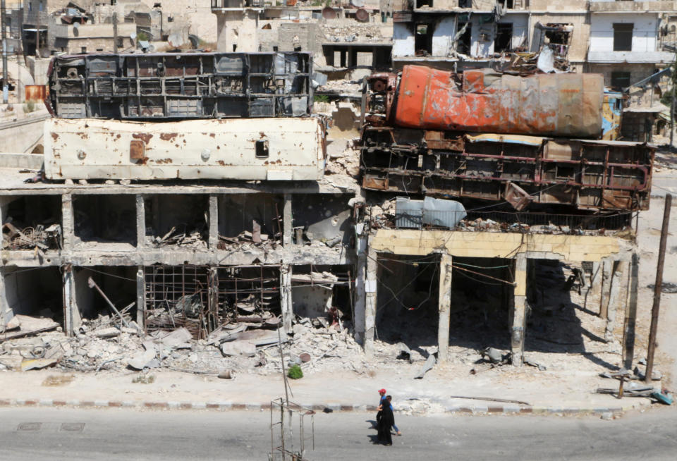 People walk past damaged buses positioned atop a building as barricades in the rebel-held Bab al-Hadid neighbourhood of Aleppo, Syria on Aug. 18, 2016.