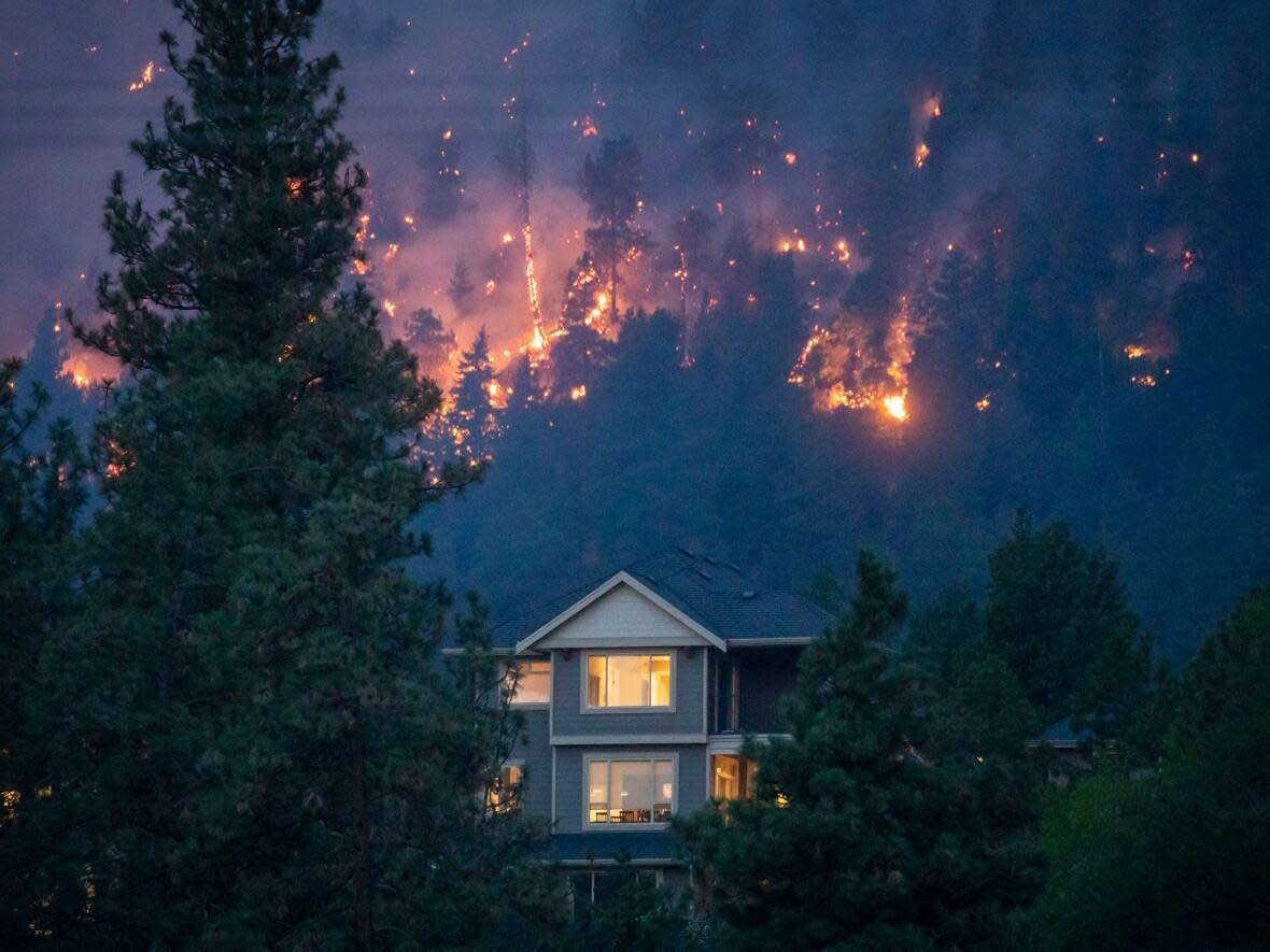 A wildfire burns near a home in the city of Kelowna, B.C., on Aug. 18, 2023. An internal RCMP report warns that a series of geopolitical and national threats — including climate change — will test the ability of governments and police services to protect Canadians in the coming years. (Ben Nelms/CBC - image credit)