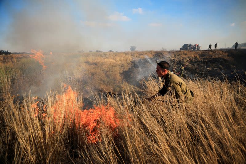 Israeli soldiers try to extinguish fire, on the Israeli side of the border between Israel and the Gaza Strip