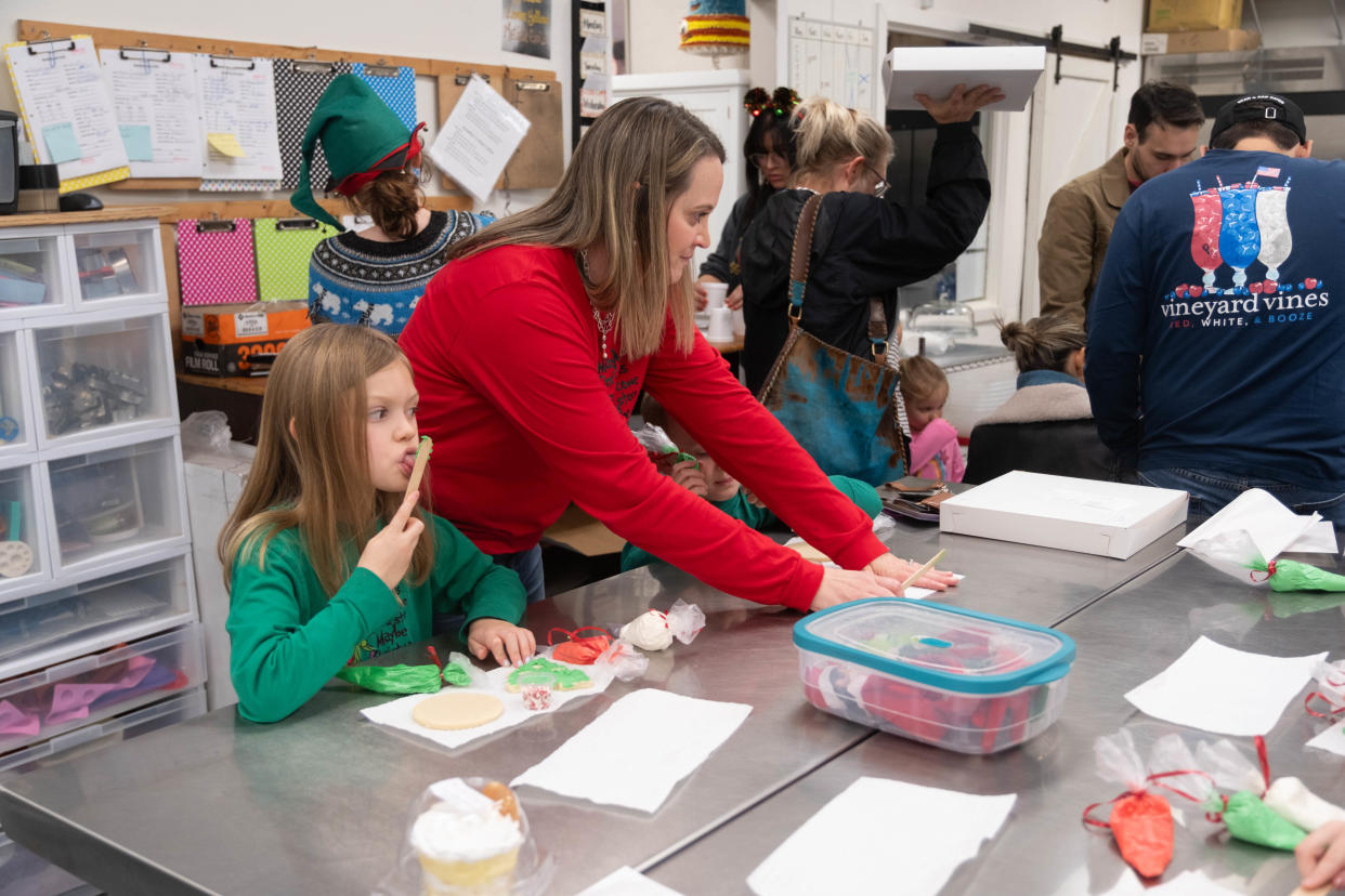 A young tests the frosting flavor as she decorates a cookie for Santa Saturday at the Cake Company of Canyon.