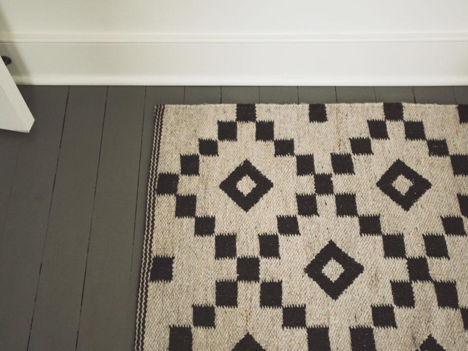 A tan and dark-brown rug with a pattern made of squares against a wooden floor