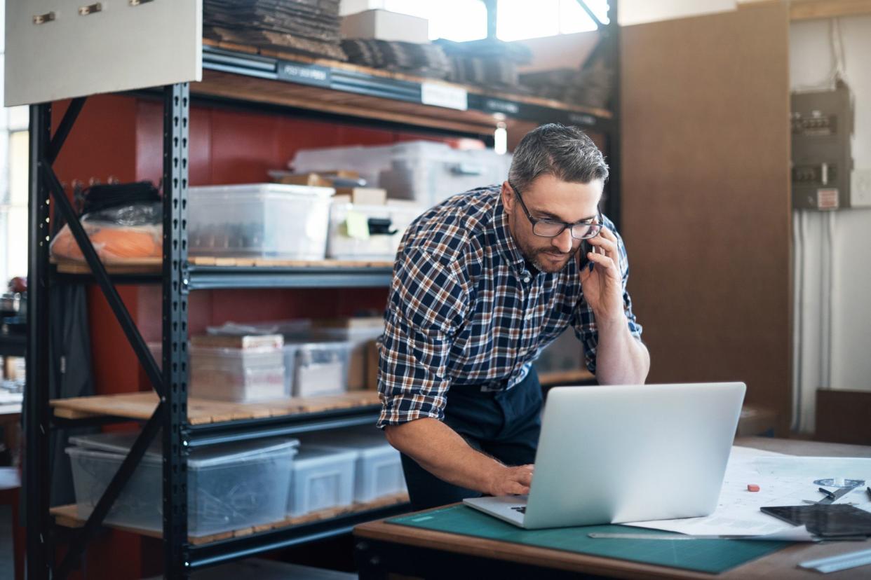 man in workshop looking at laptop looking at phone