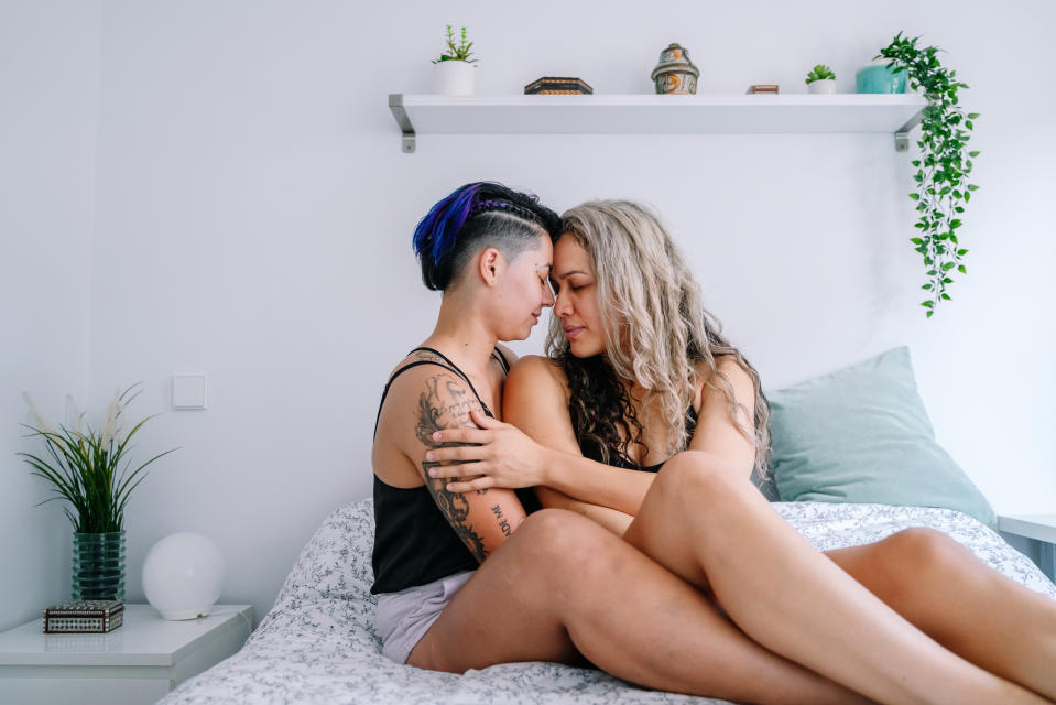 Horizontal full length view of lesbian couple in love in white bedroom with plants. Homosexual people lifestyle at home