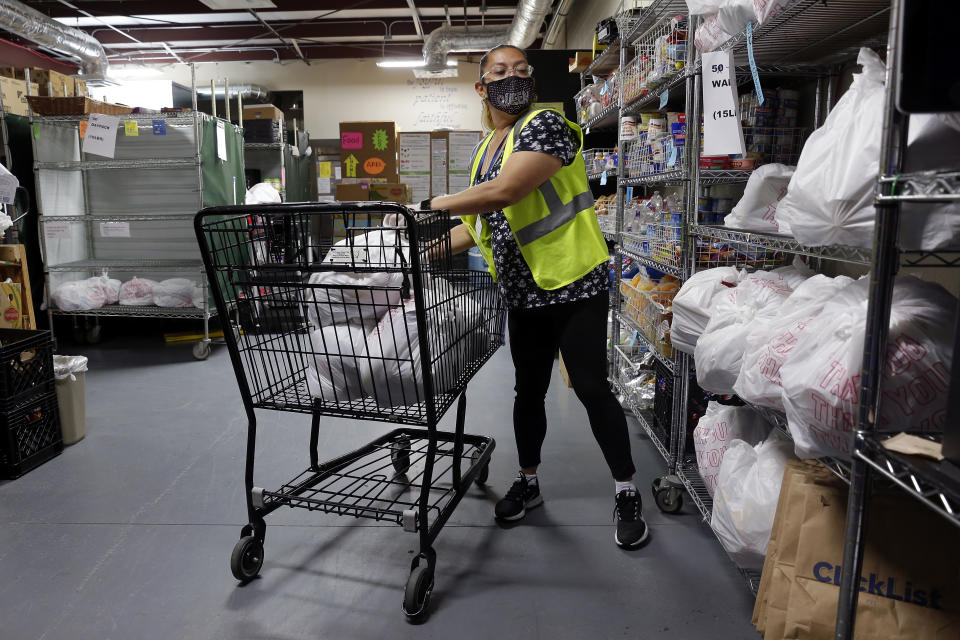 Evelyn Gomez places pre-filled bags of groceries from the indoor pantry into a shopping cart to easily take them outside to the drive thru distribution line at the West Houston Assistance Ministries Wednesday, Oct. 14, 2020, in Houston. WHAM is one of the many distribution points that gets food from the Houston Food Bank and other retail contributors to those in need around the 18 counties served by the food bank. (AP Photo/Michael Wyke)