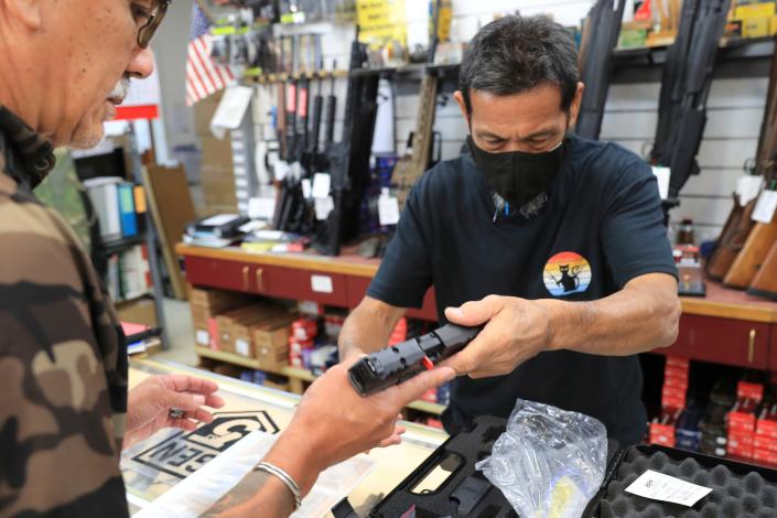 A clerk hands a gun to a customer inside a gun shop on June, 23, 2022, in Honolulu.