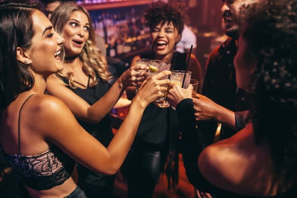 A group of people at a bar holding drinks and toasting.