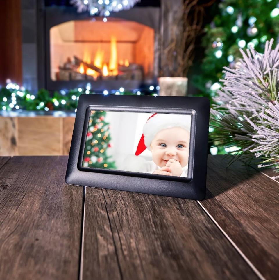 Digital black photo frame with picture of baby in a Santa hat, sitting on dark wooden table