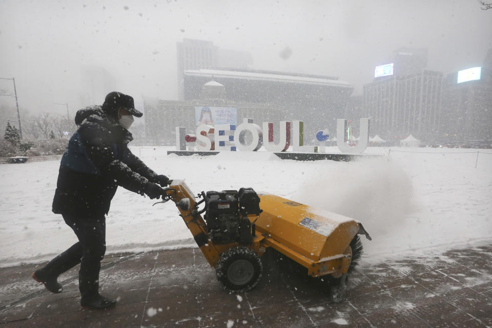 A worker wearing a face mask as a precaution against the coronavirus uses a snow blower to clear the sidewalks along City Hall Plaza in Seoul, South Korea, Tuesday, Jan. 12, 2021. (AP Photo/Ahn Young-joon)