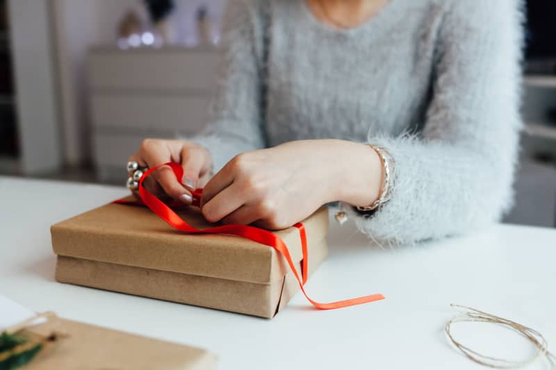 woman wearing gray fuzzy sweater wrapping a gift with red ribbon