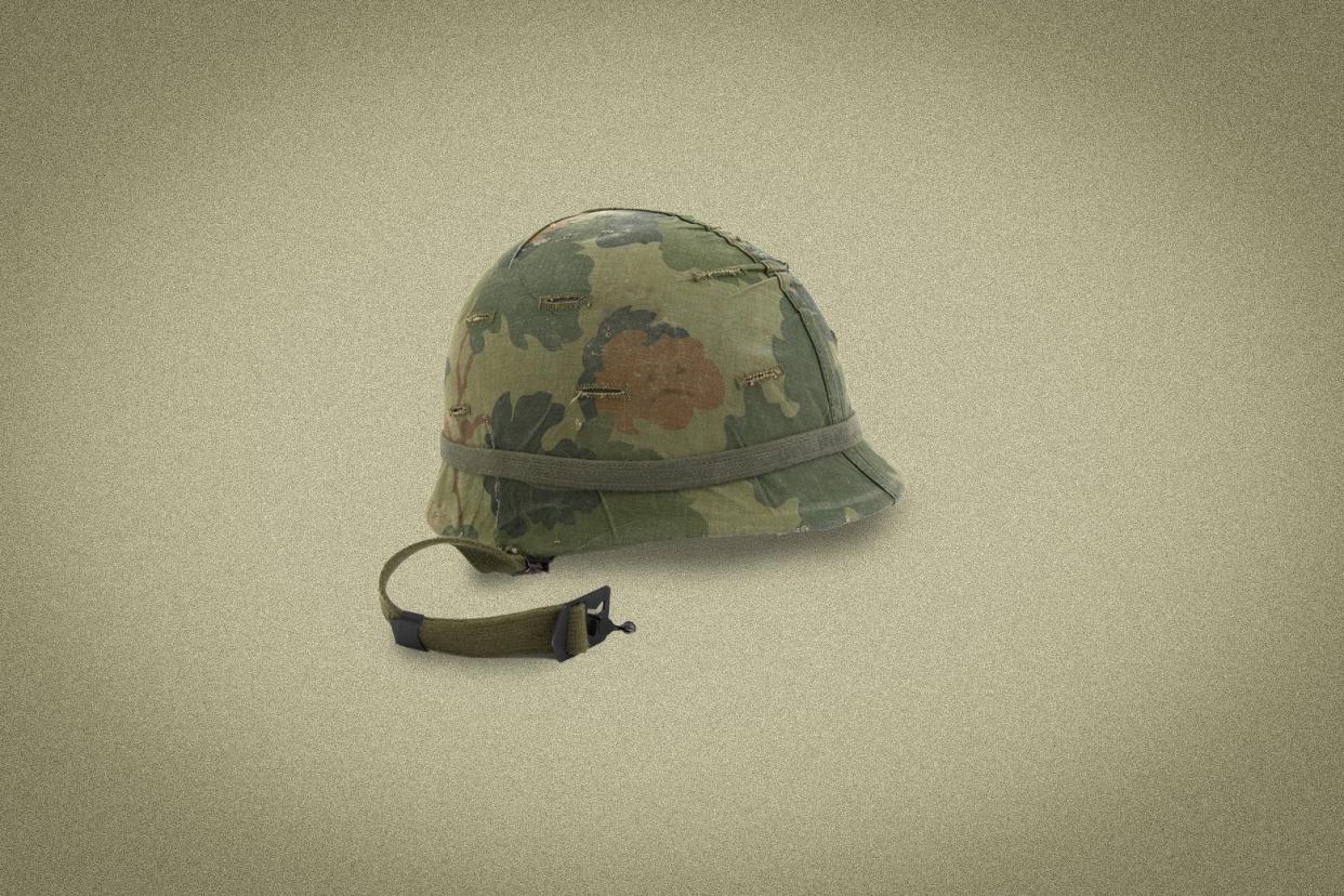 A scuffed camo military helmet has a broken strap. 