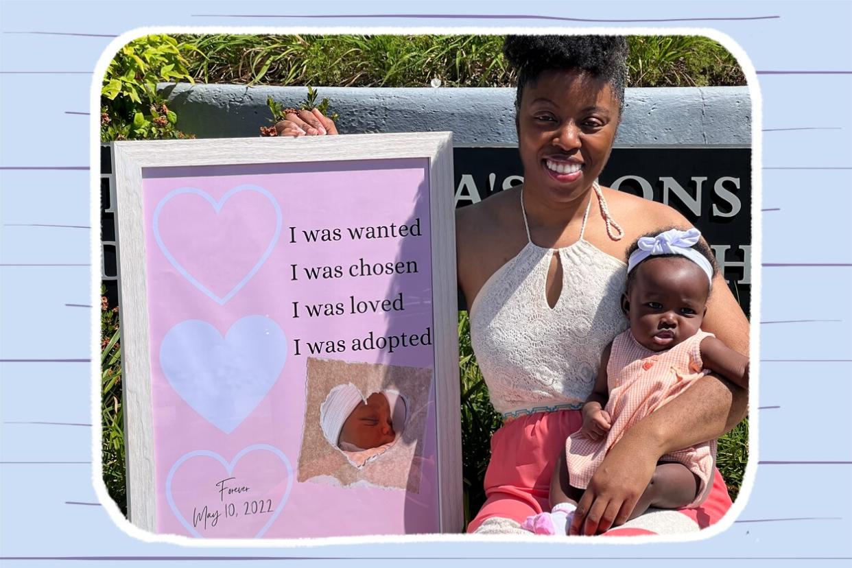 Black mom holds infant daughter outside with sign announcing her adoption.