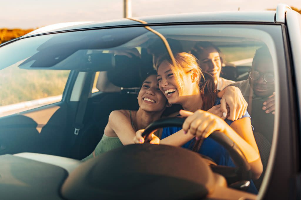 A group of teen drive in a car while hugging and smiling. 