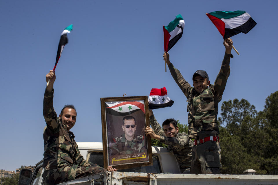 FILE - Syrian soldiers hold up Baath party flags and a portrait of Syrian President Bashar Assad with Arabic that reads "Yes to the leader of victory," as they celebrate outside the town of Douma, in the eastern Ghouta region, near the Syrian capital Damascus, Syria, Wednesday, May 26, 2021. With its war on Ukraine now in its third week, Russian President Vladimir Putin on Friday, March 11, 2022, approved bringing in volunteer fighters from the Middle East into the conflict. (AP Photo/Hassan Ammar, File)