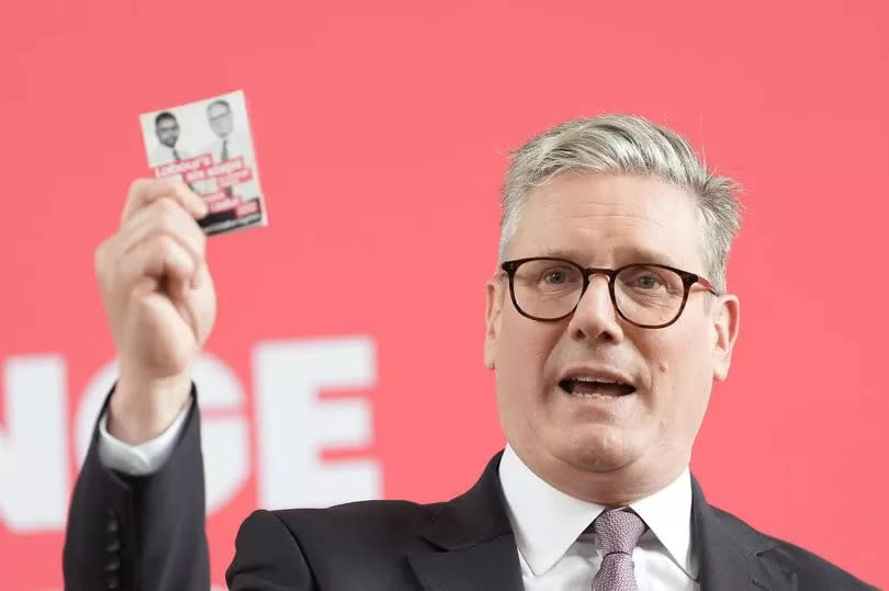 Labour leader Keir Starmer holds a pledge card with his, and Vaughan Gething's joint photo, on the front. Sir Keir is standing in front of a red background