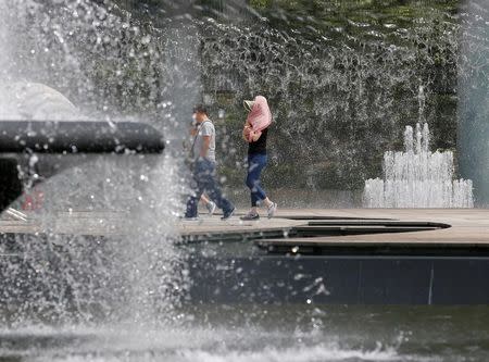 A woman shading herself from the sun, walks among fountains at a park on a hot summer day in Tokyo, Japan July 14, 2016. REUTERS/Toru Hanai