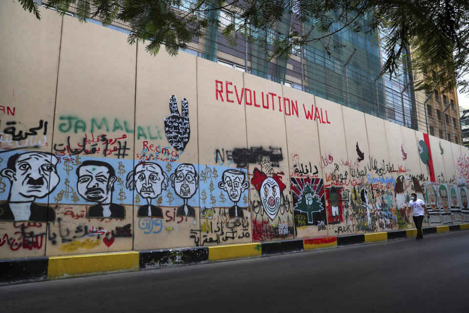 A man walks past the wall of United Nations Headquarters, decorated with graffitis painting in Beirut, Lebanon, Monday, Oct. 12, 2020. A year ago, hundreds of thousands of Lebanese took to the streets in protests nationwide that raised hopes among many for a change in a political elite that over that decades has run the country into the ground. (AP Photo/Bilal Hussein)
