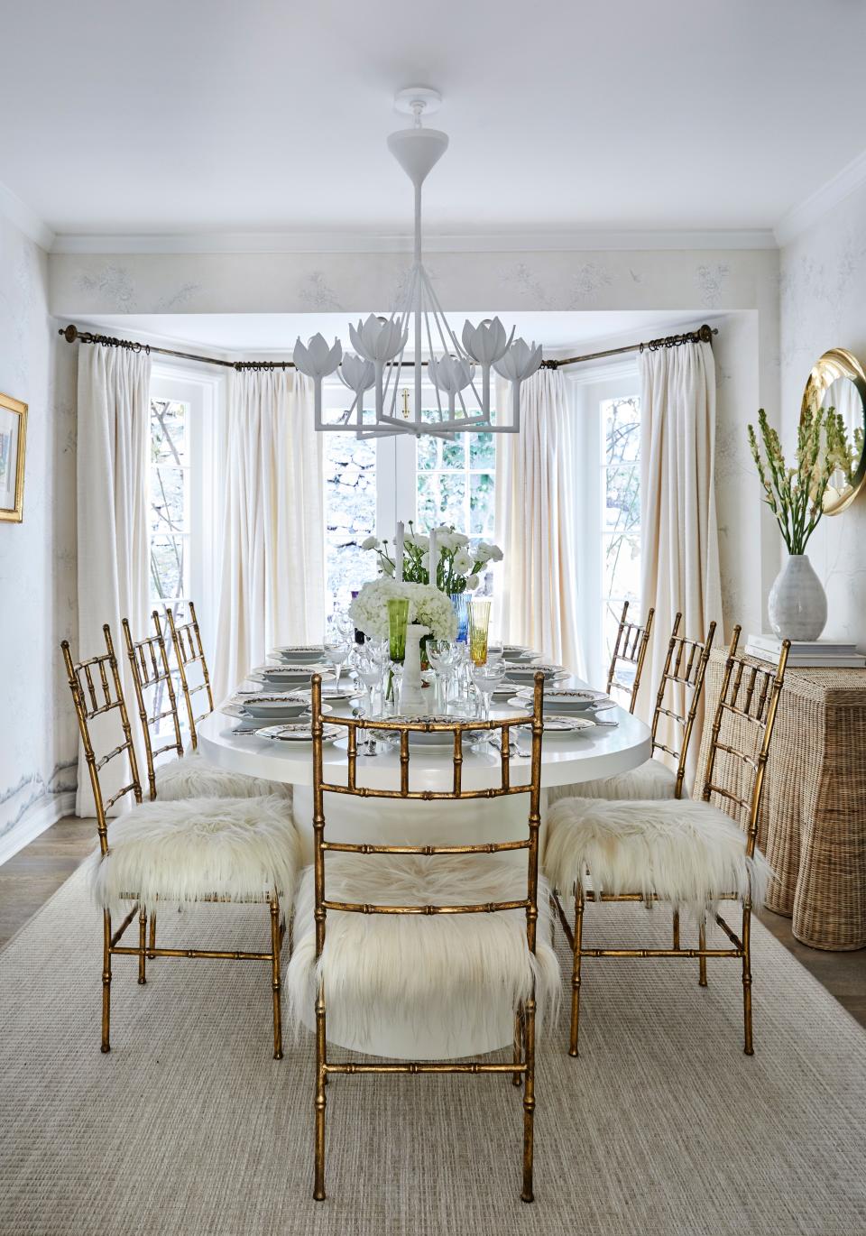 The couple’s glamorous dining room is outfitted with Galerie Glustin gilt bamboo chairs with goat hair seats around a custom white lacquer table, with an Alberto plaster chandelier by Julie Neill for Visual Comfort. Accents come by way of a rattan-skirted console Roxy found at Mainly Baskets, Pierre Frey drapes, and Gracie chinoiserie wallpaper.