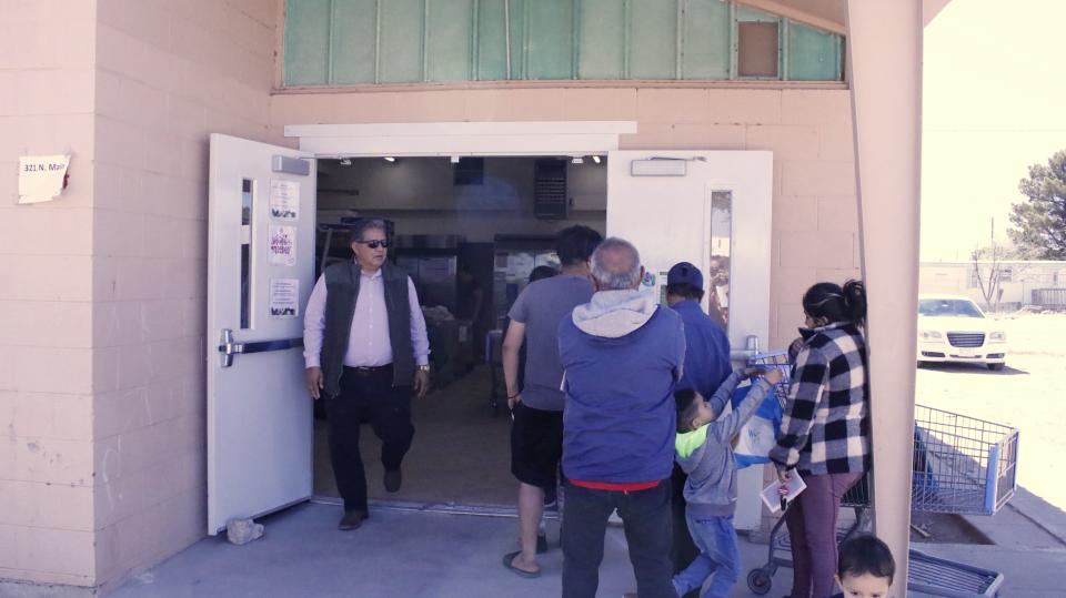 Residents, right, wait in line Wednesday, April 3, 2024, to receive emergency food assistance at a permanent pantry that opened in January in Hatch, New Mexico. Before that, a key nonprofit ran a mobile food pantry. The new facility – housed in an old school district building – expands access for area residents, says Casa de Peregrinos Executive Director Lorenzo Alba Jr., left.