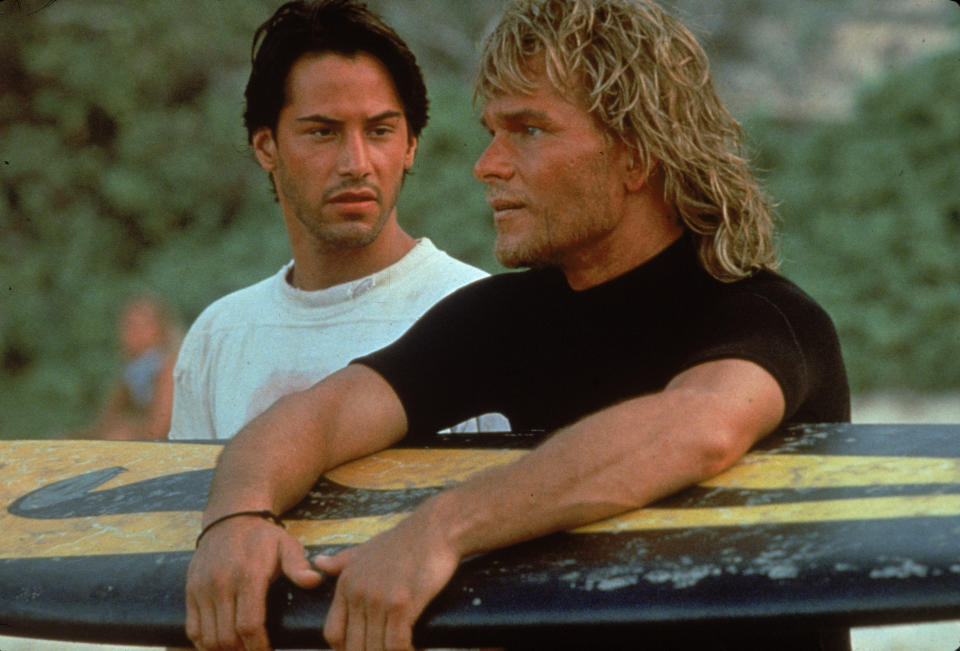 Lebanese-born American actor Keanu Reeves and American actor Patrick Swayze stand on a beach as Swayze holds a surfboard during the filming of the action movie 'Point Break' directed by Kathryn Bigelow, 1991. (Photo by Richard Foreman/Fotos International/Getty Images)