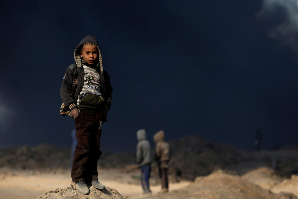 A boy stands in front of oilfields in Qayyara