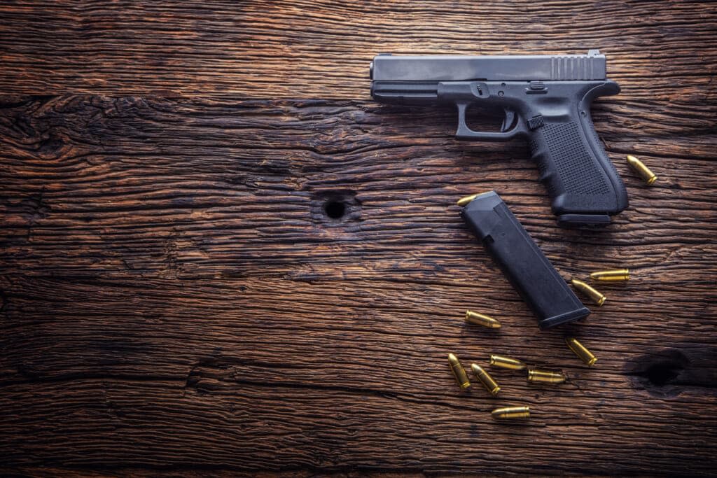 Gun pistol. 9 mm pistol gun and bullets strewn on the rustic oak table. (Adobe Stock)
