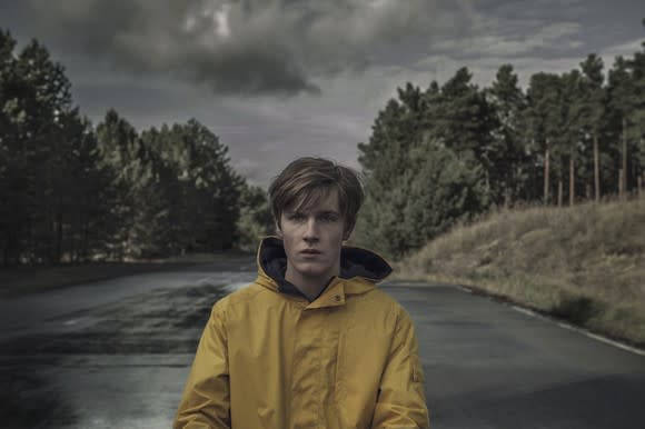 A person standing on a road in a yellow raincoat in a scene from Netflix original Dark.