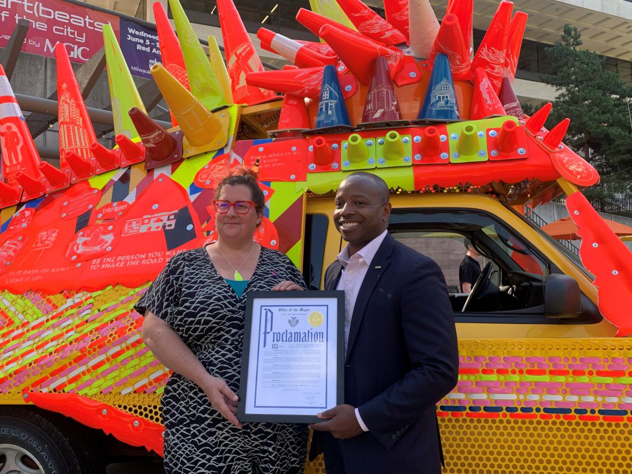 Mayor Cavalier Johnson and artist Sarah Davitt holding honorable proclamation in front of 'The Moving City' truck at Red Arrow Park.