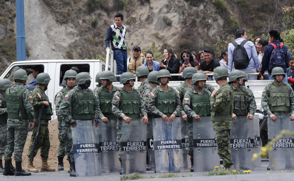 Gente que se transporta en la parte trasera de un camión observa mientras soldados montan guardia para mantener los caminos abiertos en la autopista Simón Bolívar en Quito, Ecuador, el lunes 7 de octubre de 2019. (AP Foto/Dolores Ochoa)