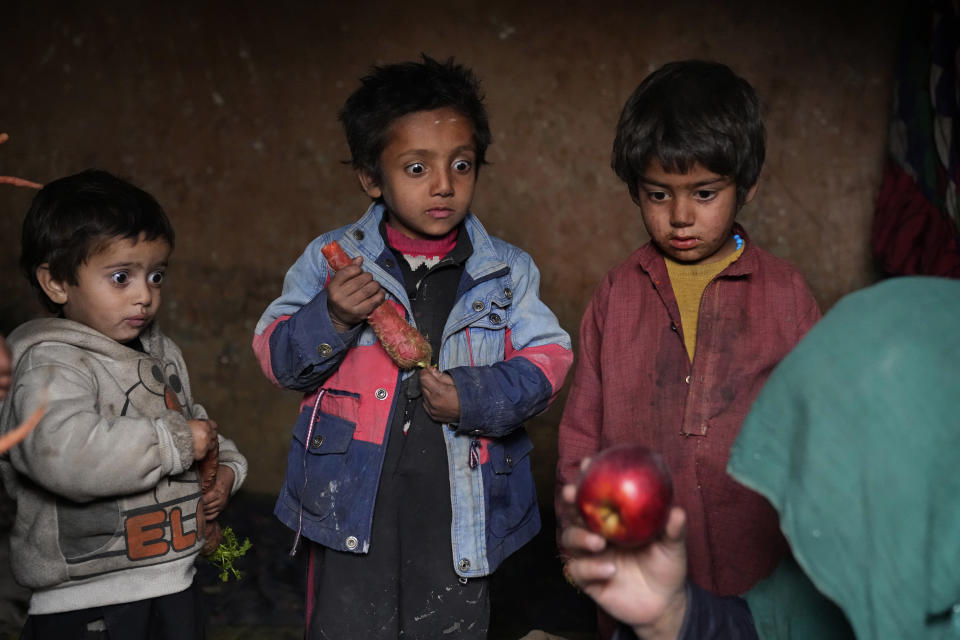 Esta imagen proporcionada por World Press Photo forma parte de una serie titulada "Afganistán en vilo", que ganó la categoría de Serie en Asia de World Press Photo. Desde la caótica toma talibán de Kabul el 15 de agosto de 2021, una economista ya devastada por la guerra y que sólo se mantenía en marcha por donaciones internacionales se ve ahora al borde del colapso. No hay dinero suficiente para los hospitales. La Organización Mundial de la Salud alerta que millones de niños sufren malnutrición y la ONU estima que el 97% de los afganos pronto vivirán bajo el umbral de la pobreza. En la imagen, tres niños desplazados miran con sorpresa una manzana que su madre llevó a casa tras mendigar, en un campamento a las afueras de Kabul, Afganistán, el jueves 2 de febrero de 2023. (AP Foto/Ebrahim Noroozi)