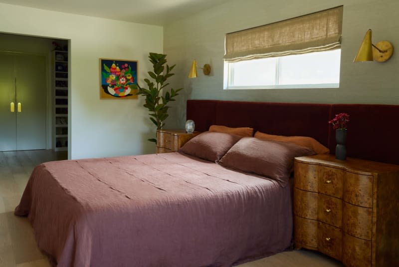 Light sage green wall, maroon bedding, maroon long wall mounted headboard, vintage wood curved night stand