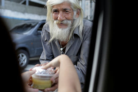 Una voluntaria de "Haz La Diferencia" le da a través de una ventanilla de un automóvil una taza de sopa a un hombre sin hogar en una calle de Caracas, Venezuela March12, 2017. REUTERS/Marco Bello