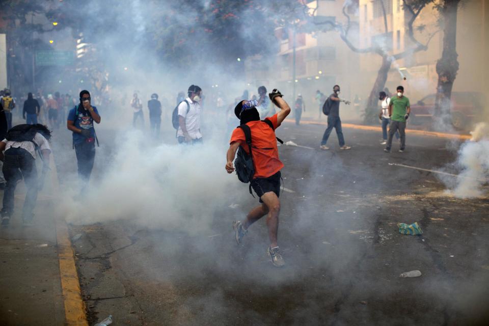 Demonstrators throw objects amid tear gas launched by the Bolivarian National Police (BNP) in the Altamira neighborhood of Caracas, Venezuela, Wednesday, Feb. 19, 2014. Venezuelan security forces backed by water tanks and tear gas dispersed groups of anti-government demonstrators who tried to block Caracas' main highway Wednesday evening. (AP Photo/Rodrigo Abd)