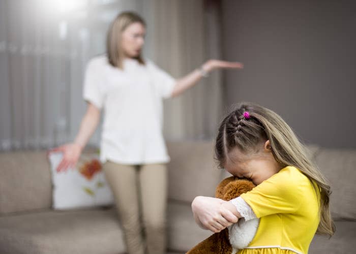 Adult gesturing to a child hugging a toy, implying a time-out or discipline scenario