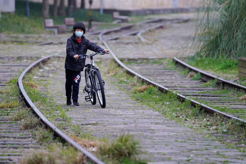 A boy wearing a face mask walks with his bicycle at a park as the country is hit by an outbreak of the novel coronavirus, in Shanghai