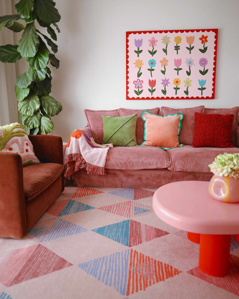 White living room with rose colored sofa, pink and red coffee table, and pink, blue and red patterned rug