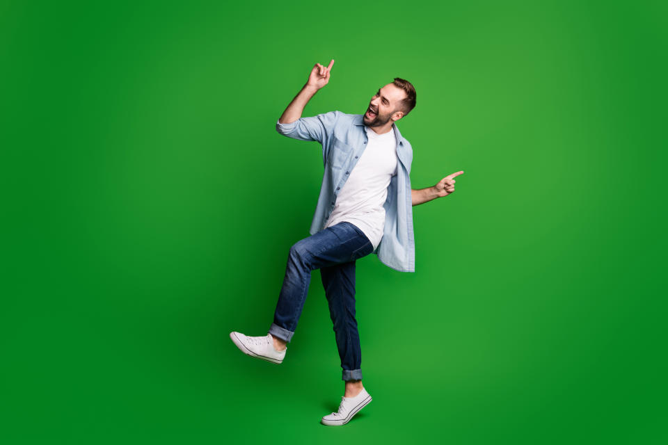 A joyful man in casual attire dancing with a victory sign on a green background