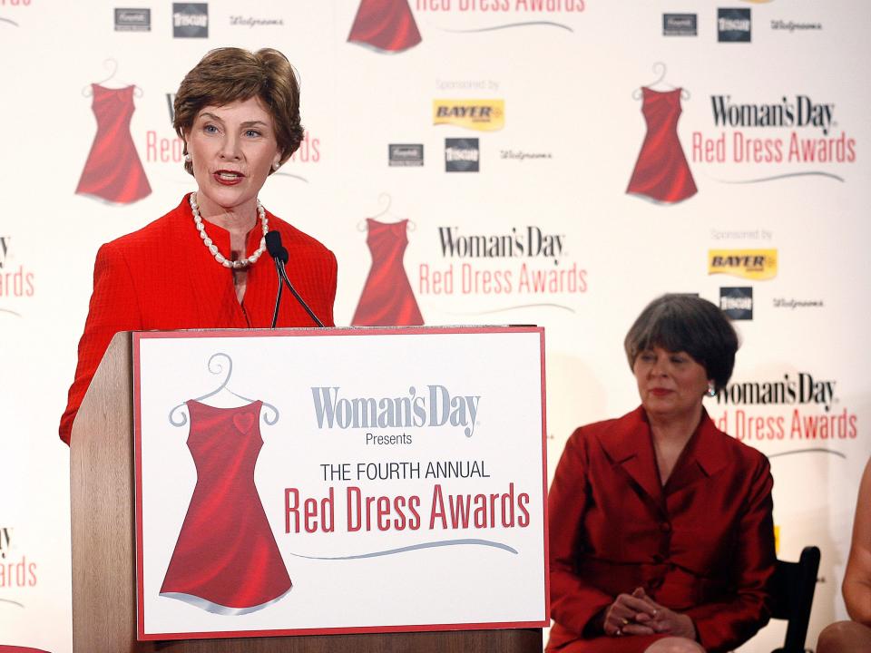 Laura Bush dressed in a red suit is speaking at a podium at the fourth annual Red Dress Awards.