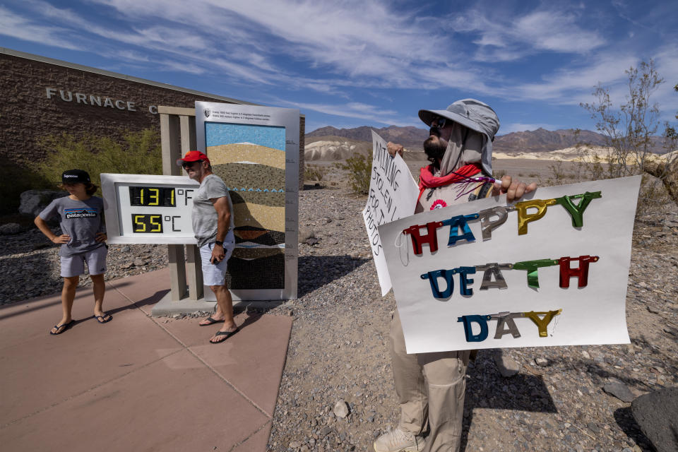 Tom Comitta holds two signs, one of which reads Happy Death Day, while the thermometer registers 131 degrees Fahrenheit, the equivalent of 55 degrees Celsius.