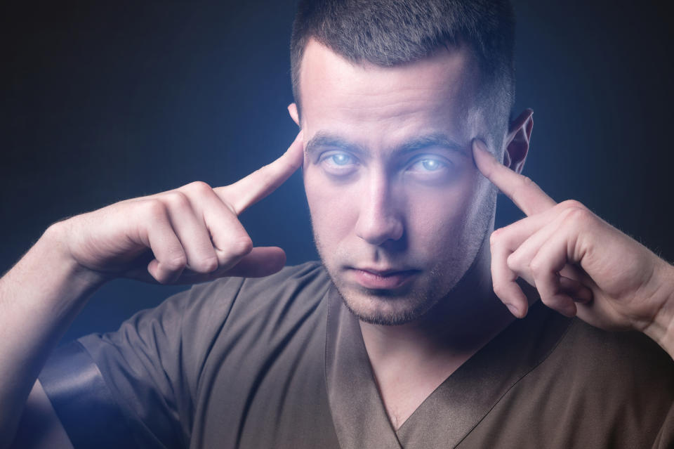 A man is focusing with his fingers on his temples, looking intensely at the camera. His brows are furrowed and he is wearing a V-neck shirt